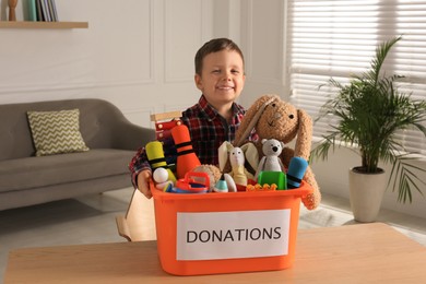 Cute little boy holding donation box with toys at home