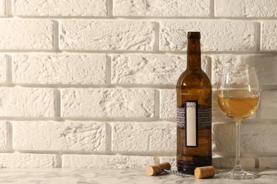 Bottle and glass of wine on white marble table near brick wall. Space for text