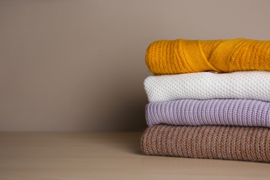 Stack of folded knitted sweaters on wooden table. Space for text