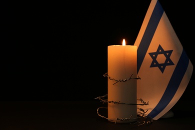 Flag of Israel, barbed wire and burning candle on black background, space for text. Holocaust memory day