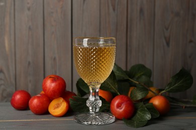 Delicious plum liquor and ripe fruits on grey wooden table. Homemade strong alcoholic beverage