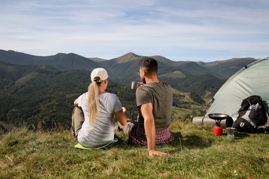 Couple enjoying mountain landscape near camping tent, back view