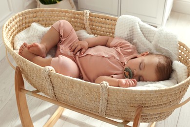 Cute little baby with pacifier sleeping in wicker crib at home