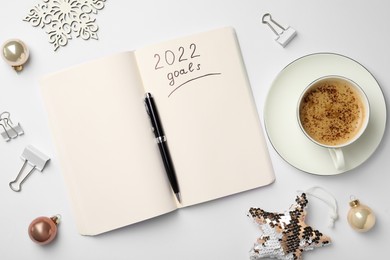 Inscription 2022 Goals written in planner, cup of coffee and Christmas decor on white background, flat lay. New Year aims