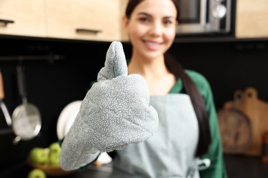 Photo of Woman in apron and oven glove showing thumb up indoors, focus on hand. Space for text