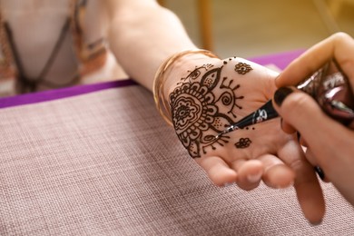 Professional mehndi master making henna tattoo at table, closeup. Space for text