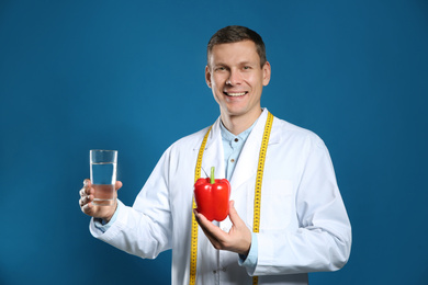 Nutritionist with glass of water and bell pepper on blue background