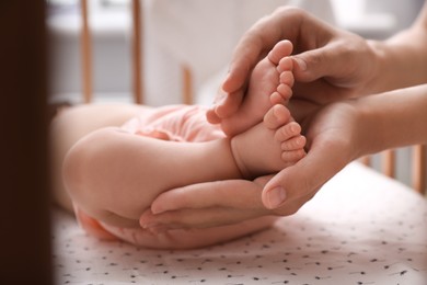 Mother holding feet of her cute sleeping baby at home, closeup