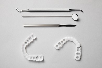 Photo of Bite correction. Mouth guards and dentist tools on light grey background, flat lay