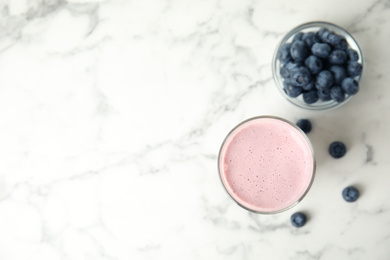 Tasty milk shake and blueberries on white marble table, flat lay. Space for text