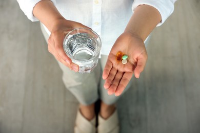 Photo of Young woman with glass of water and dietary supplement pills indoors, above view