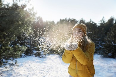 Woman blowing snow from hands in winter forest, space for text