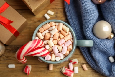 Flat lay composition with cup of tasty cocoa, candy canes and Christmas gifts on wooden table, flat lay