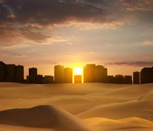 Sandy desert and silhouette of city on horizon at sunset