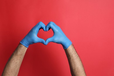 Doctor in medical gloves making heart with hands on red background, closeup. Space for text