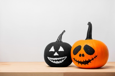 Halloween celebration. Pumpkins with drawn faces on wooden table against light grey background, space for text