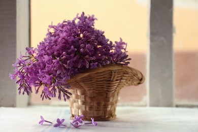 Beautiful lilac flowers in wicker basket on window sill indoors