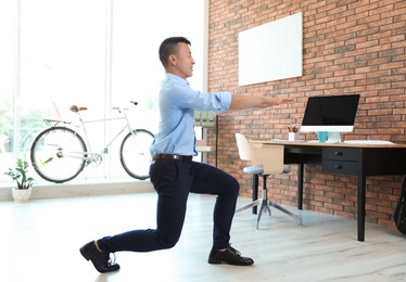 Young businessman doing exercises in office. Workplace fitness