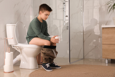 Boy with paper suffering from hemorrhoid on toilet bowl in rest room