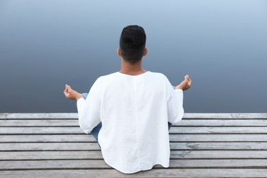 Man meditating on wooden pier near river, back view