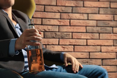 Addicted man with bottle of alcoholic drink near red brick wall, closeup. Space for text