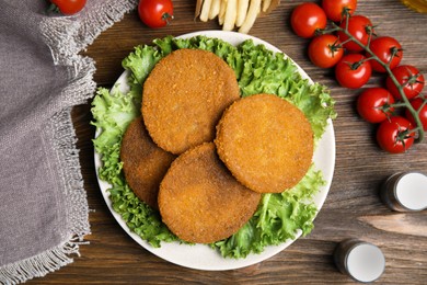 Delicious fried breaded cutlets, spices and cherry tomatoes on wooden table, flat lay