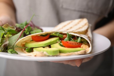 Woman holding plate with delicious hummus wraps and vegetables, closeup