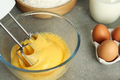 Photo of Beating eggs in glass bowl with mixer on light grey table, closeup