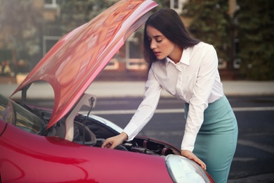 Photo of Stressed woman fixing broken car on city street