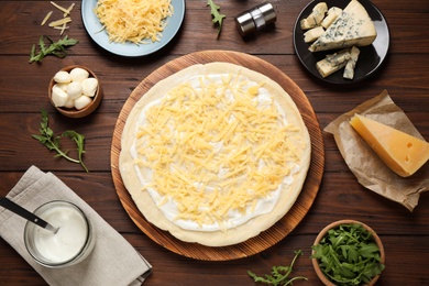 Flat lay composition with pizza crust and ingredients on wooden table