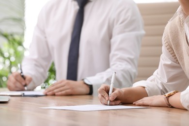 Woman signing contract at table in office, closeup.