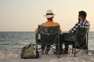 Couple sitting in camping chairs and enjoying seascape on beach, back view