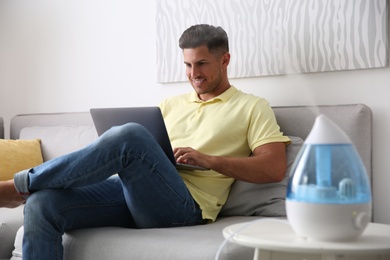 Man using laptop in room with modern air humidifier