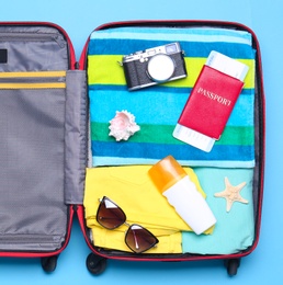 Open suitcase with beach objects on blue background, top view