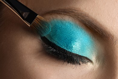 Applying cyan eye shadow onto woman's face, closeup. Beautiful evening makeup