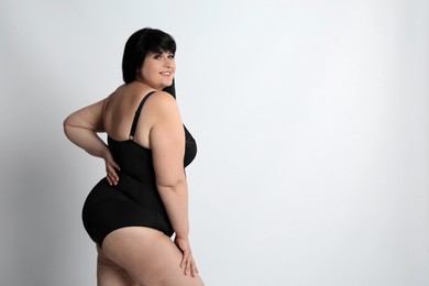 Beautiful overweight woman in black underwear on light background, space for text. Plus-size model