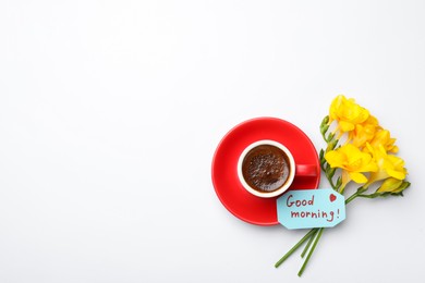 Cup of aromatic coffee, beautiful yellow freesias and Good Morning note on white background, flat lay. Space for text