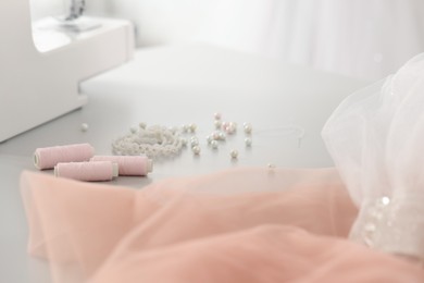 Photo of Sewing machine, fabric, threads and white beads on table in atelier, closeup