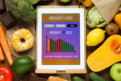 Photo of Tablet with weight loss calculator application and food products on wooden table, flat lay