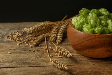 Photo of Fresh green hops, wheat grains and spikes on wooden table, space for text