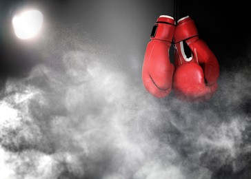 Pair of boxing gloves and white smoke illuminated by spotlight on dark background