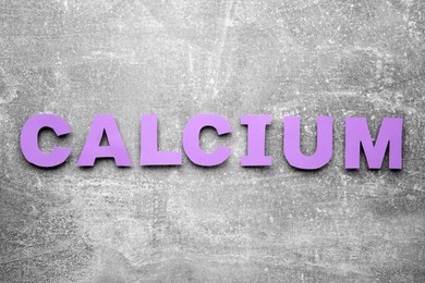Word Calcium made of violet paper letters on gray background, top view