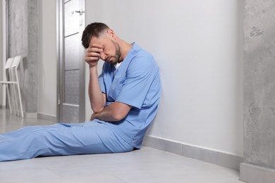 Photo of Exhausted doctor sitting near grey wall in hospital corridor
