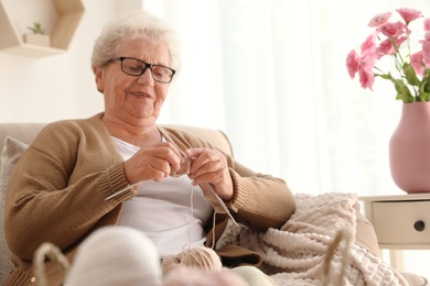 Elderly woman knitting at home. Creative hobby