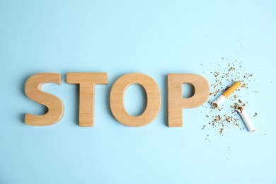 Broken cigarette near word Stop made with wooden letters on light blue background, flat lay. Quitting smoking concept