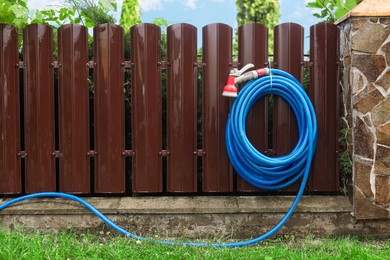 Watering hose with sprinkler hanging on wooden fence in garden, space for text
