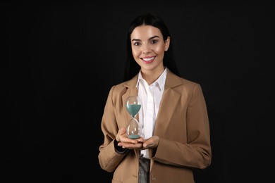 Businesswoman holding hourglass on black background. Time management