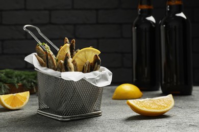 Photo of Delicious fried anchovies with slices of lemon on grey table. Space for text