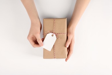 Woman holding parcel wrapped in kraft paper with tag on white background, top view