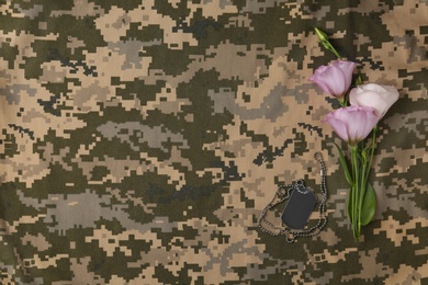 Fresh flowers and ID tag on camouflage background, flat lay with space for text. Armed Forces Day